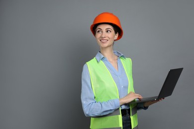 Photo of Engineer in hard hat with laptop on grey background, space for text