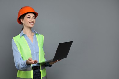 Engineer in hard hat with laptop on grey background, space for text