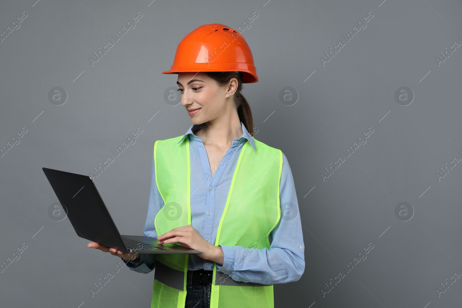 Photo of Engineer in hard hat with laptop on grey background, space for text