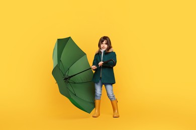 Photo of Cute little girl with green umbrella on yellow background