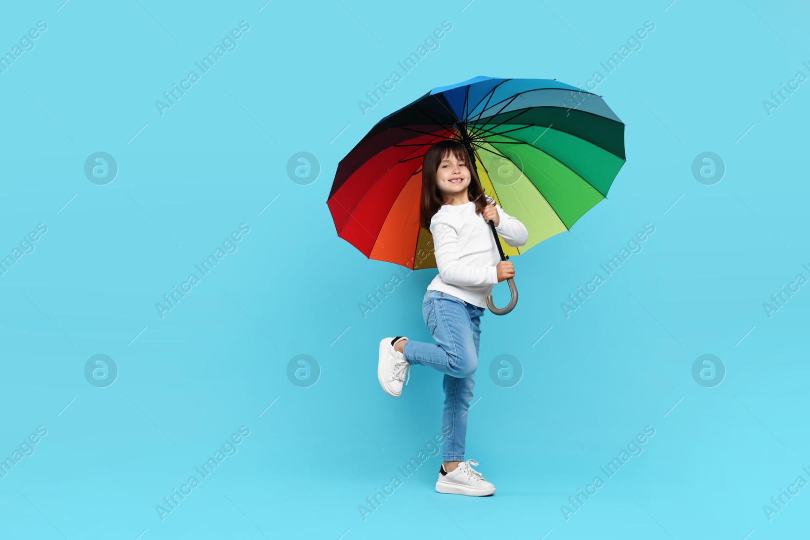 Photo of Cute little girl with colorful umbrella on light blue background. Space for text