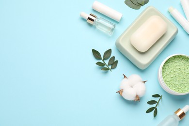 Photo of Different cosmetic products, leaves and cotton flower on light blue background, flat lay. Space for text