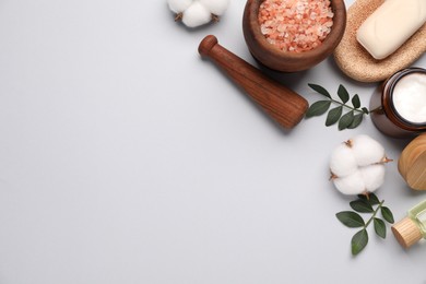 Photo of Different cosmetic products, leaves and cotton flowers on light grey background, flat lay. Space for text