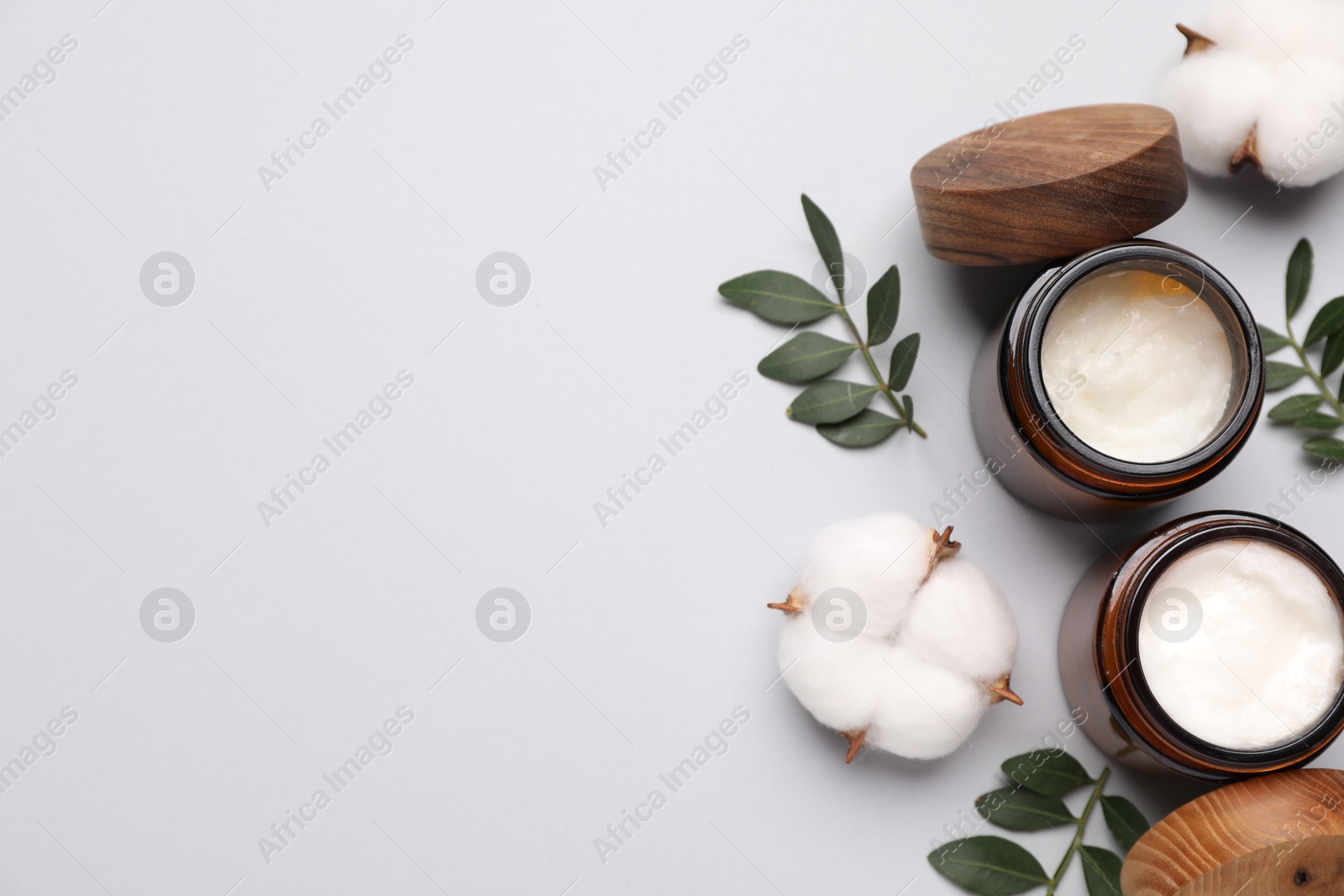 Photo of Different cosmetic products, leaves and cotton flowers on light grey background, flat lay. Space for text