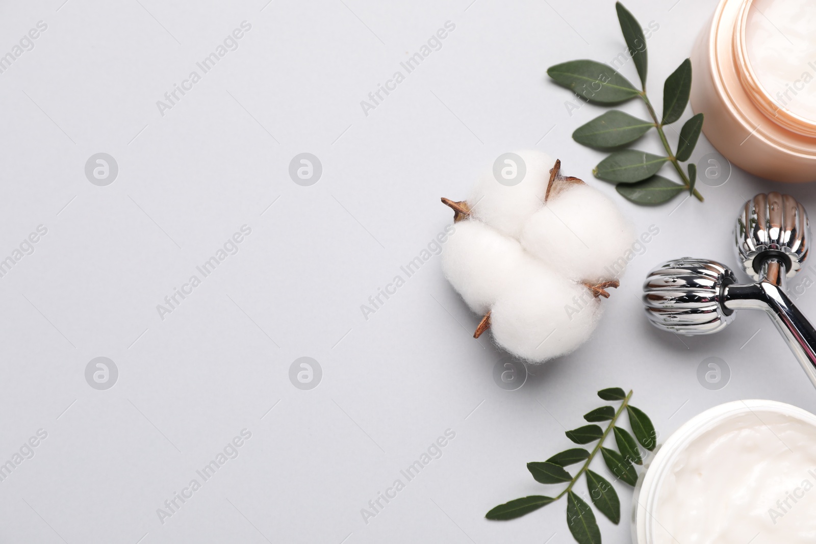 Photo of Different cosmetic products, green leaves and cotton flowers on light grey background, flat lay. Space for text