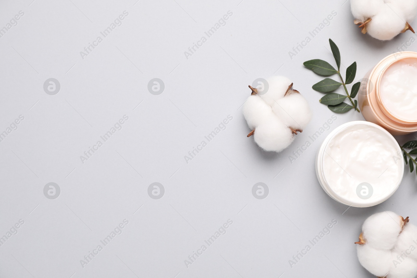 Photo of Different cosmetic products, green leaves and cotton flowers on light grey background, flat lay. Space for text