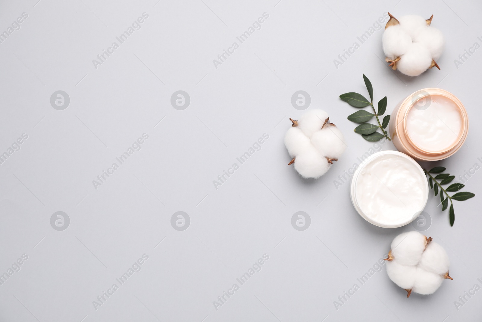 Photo of Different cosmetic products, green leaves and cotton flowers on light grey background, flat lay. Space for text