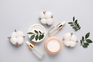 Photo of Different cosmetic products, leaves and cotton flowers on light grey background, flat lay