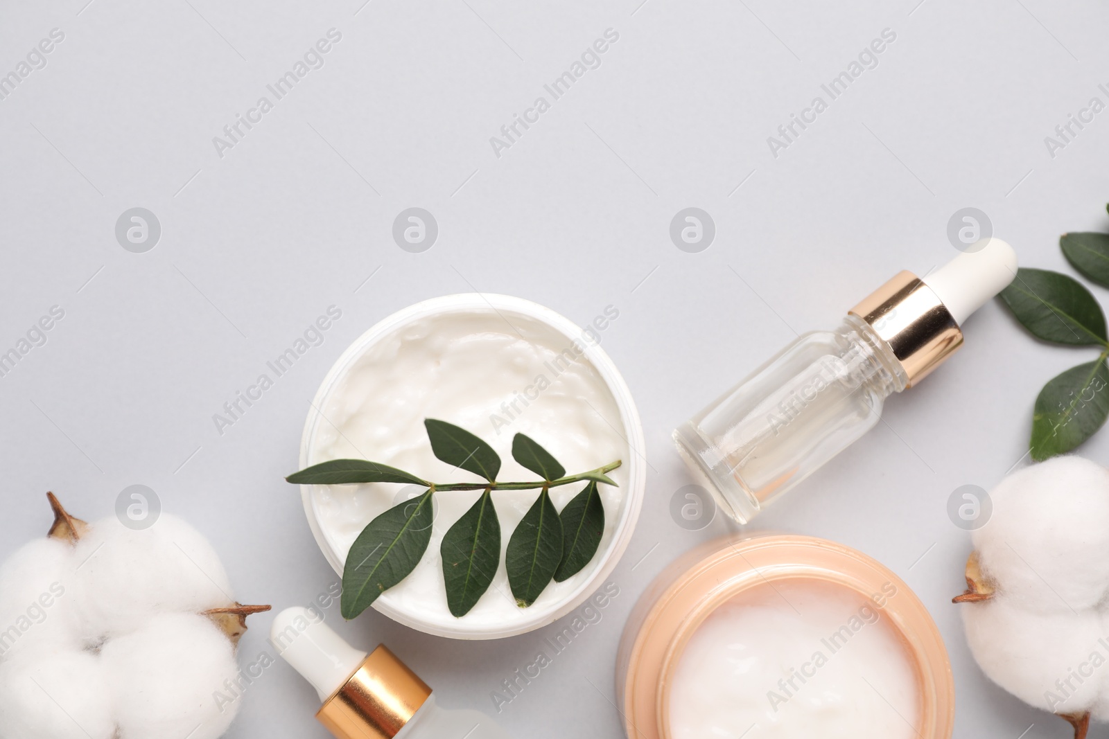 Photo of Different cosmetic products, leaves and cotton flowers on light grey background, flat lay. Space for text