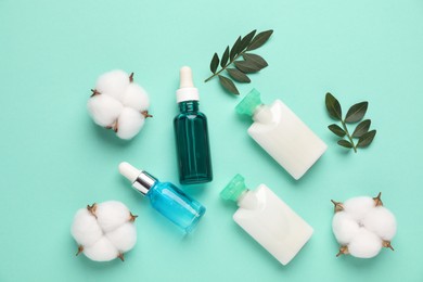 Photo of Different cosmetic products, cotton flowers and leaves on turquoise background, flat lay