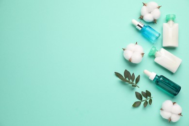 Photo of Different cosmetic products, cotton flowers and leaves on turquoise background, flat lay. Space for text