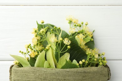 Fresh linden leaves and flowers in bag on white wooden table, top view