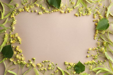 Frame of beautiful linden blossoms and green leaves on dark beige background, flat lay. Space for text