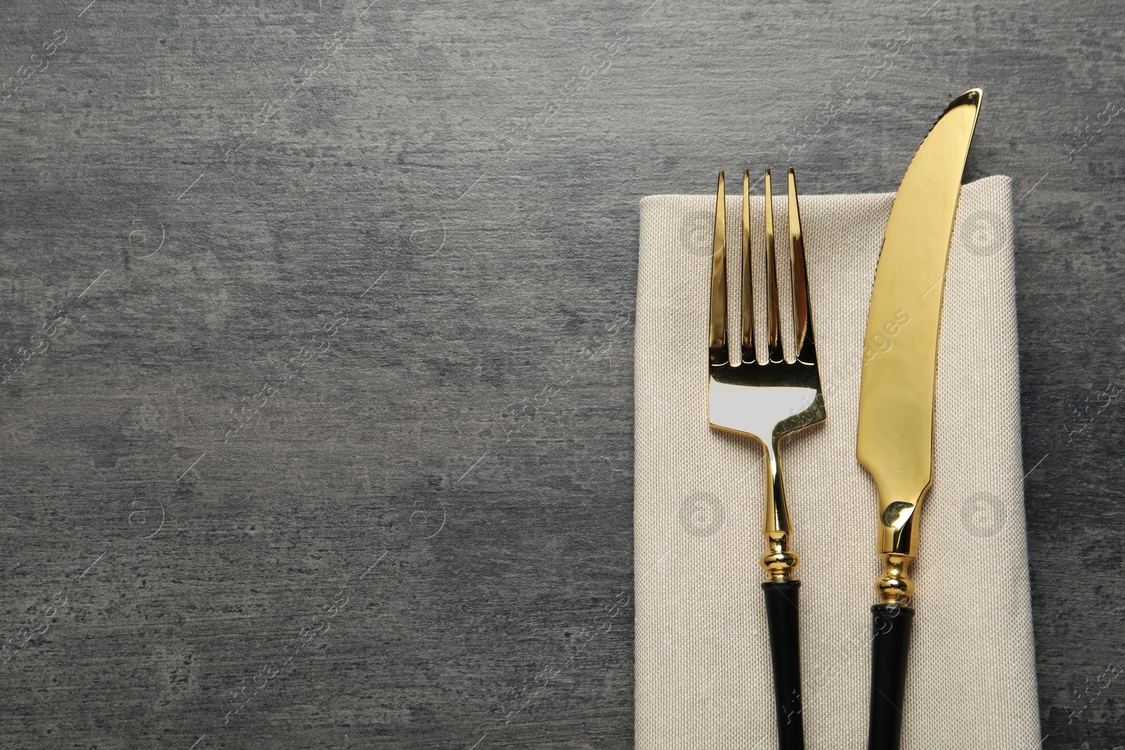 Photo of Elegant golden cutlery and napkin on grey table, top view. Space for text