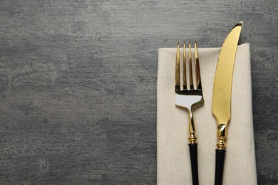 Elegant golden cutlery and napkin on grey table, top view. Space for text