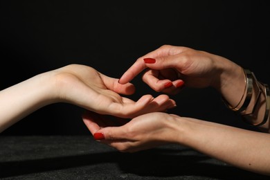 Photo of Fortune teller reading lines on woman's palm at dark grey table, closeup. Chiromancy