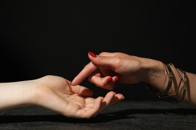 Photo of Fortune teller reading lines on woman's palm at dark grey table, closeup. Chiromancy