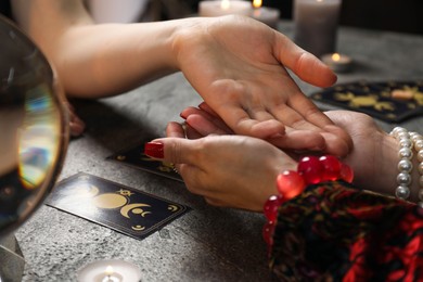 Fortune teller reading lines on woman's palm at black table, closeup. Chiromancy