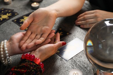 Fortune teller reading lines on woman's palm at black table, closeup. Chiromancy