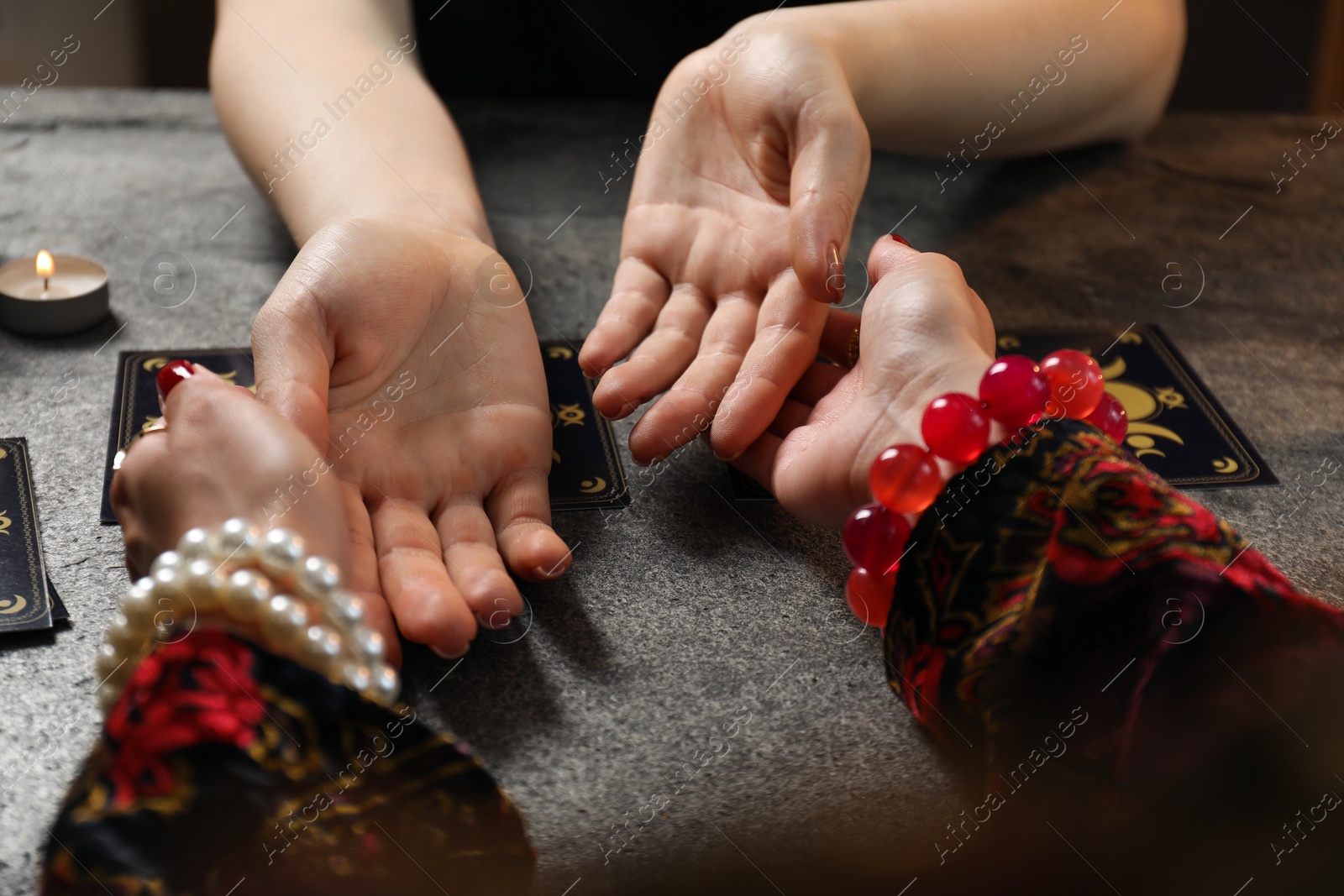 Photo of Fortune teller reading lines on woman's palm at black table, closeup. Chiromancy