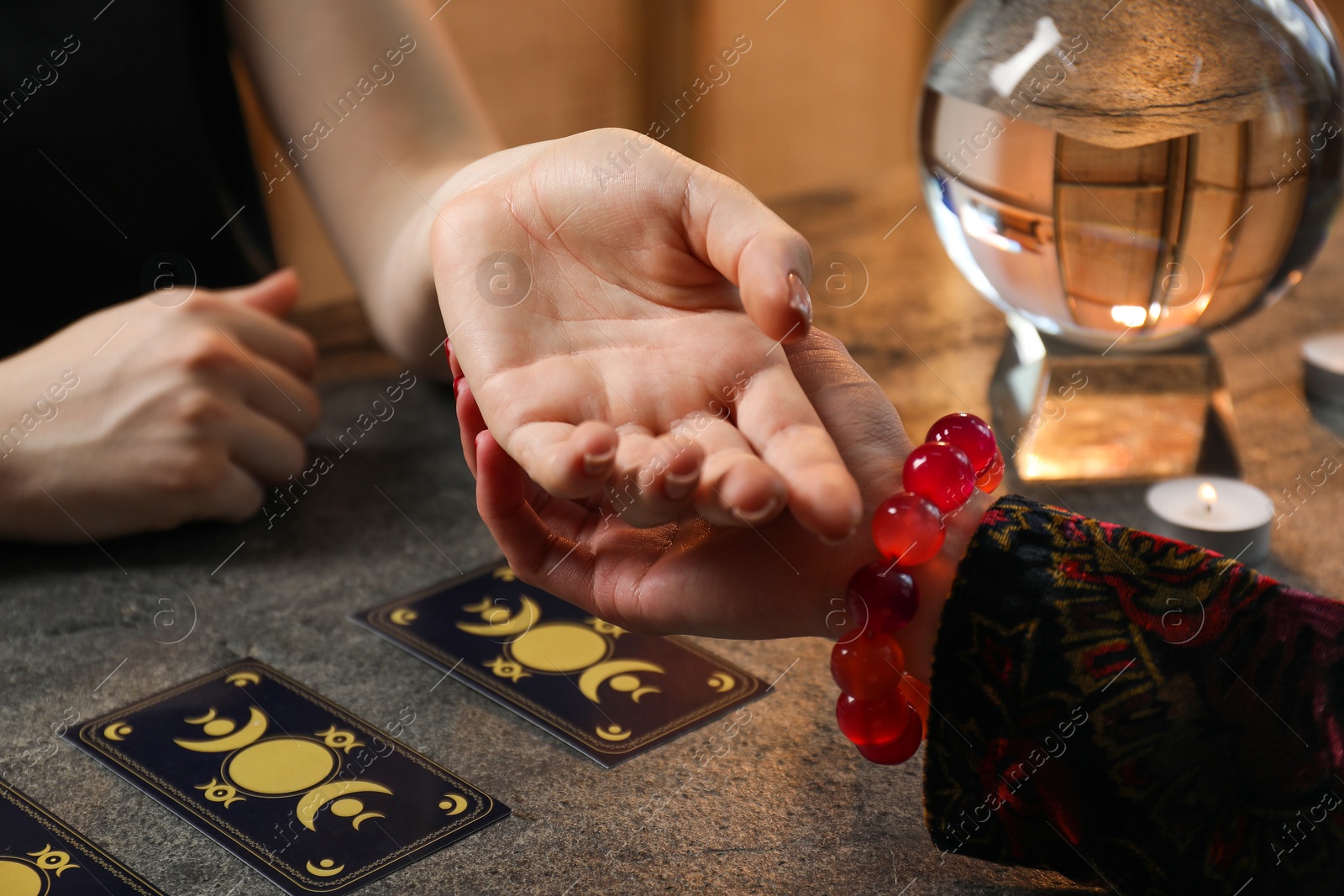 Photo of Fortune teller reading lines on woman's palm at black table, closeup. Chiromancy