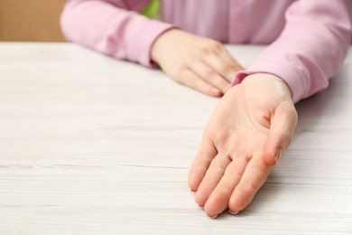 Chiromancy and foretelling. Woman showing palm at white wooden table, closeup. Space for text