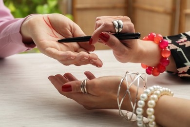 Photo of Fortune teller reading lines on woman's palm at white wooden table, closeup. Chiromancy