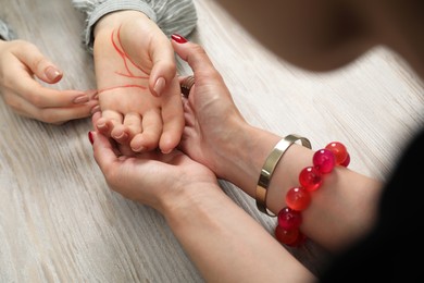 Photo of Fortune teller reading lines on woman's palm at wooden table, closeup. Chiromancy