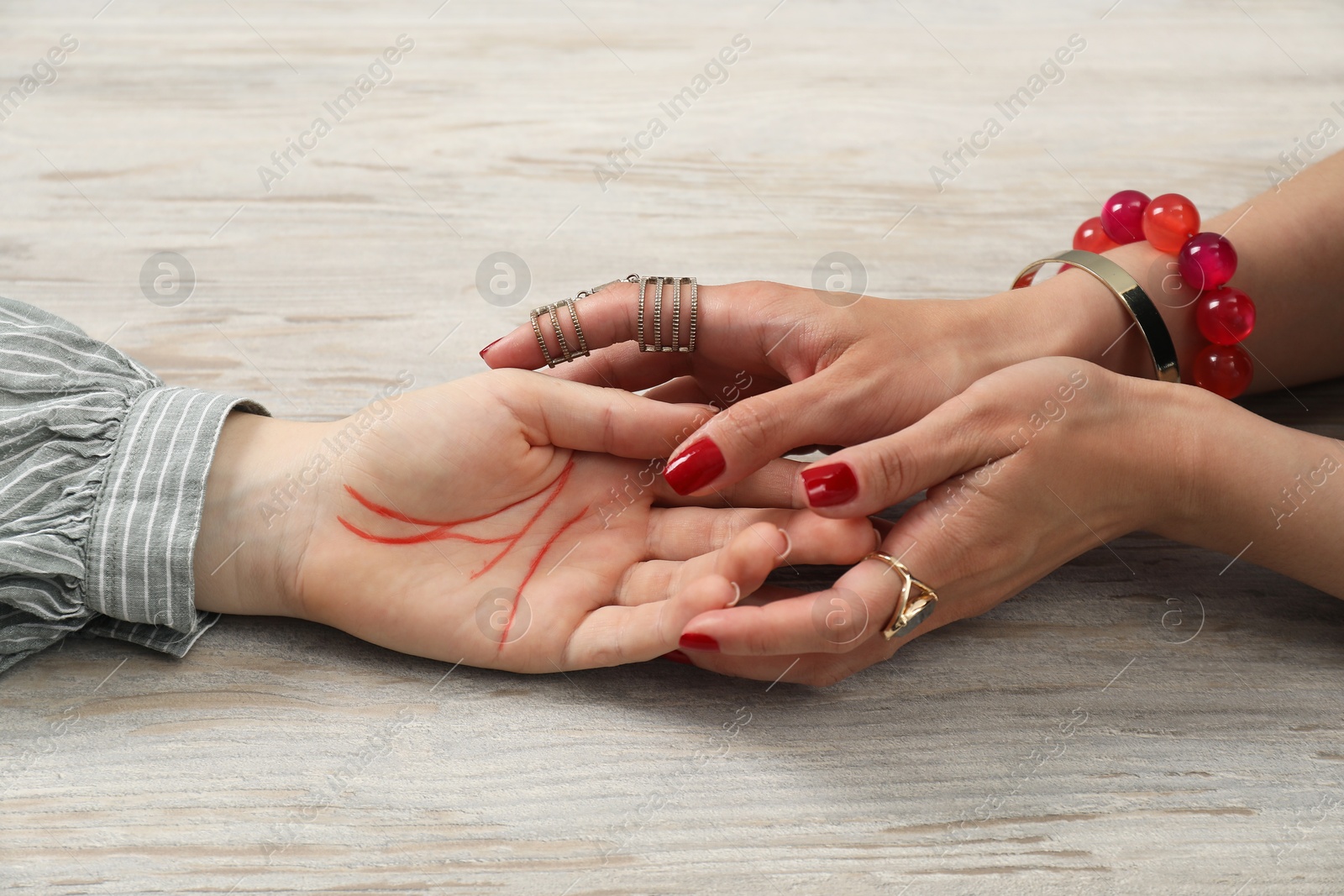 Photo of Fortune teller reading lines on woman's palm at wooden table, closeup. Chiromancy