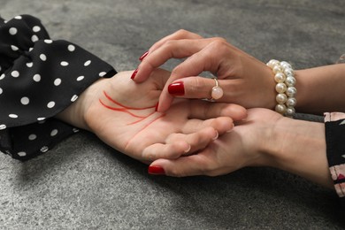 Photo of Fortune teller reading lines on woman's palm at grey table, closeup. Chiromancy