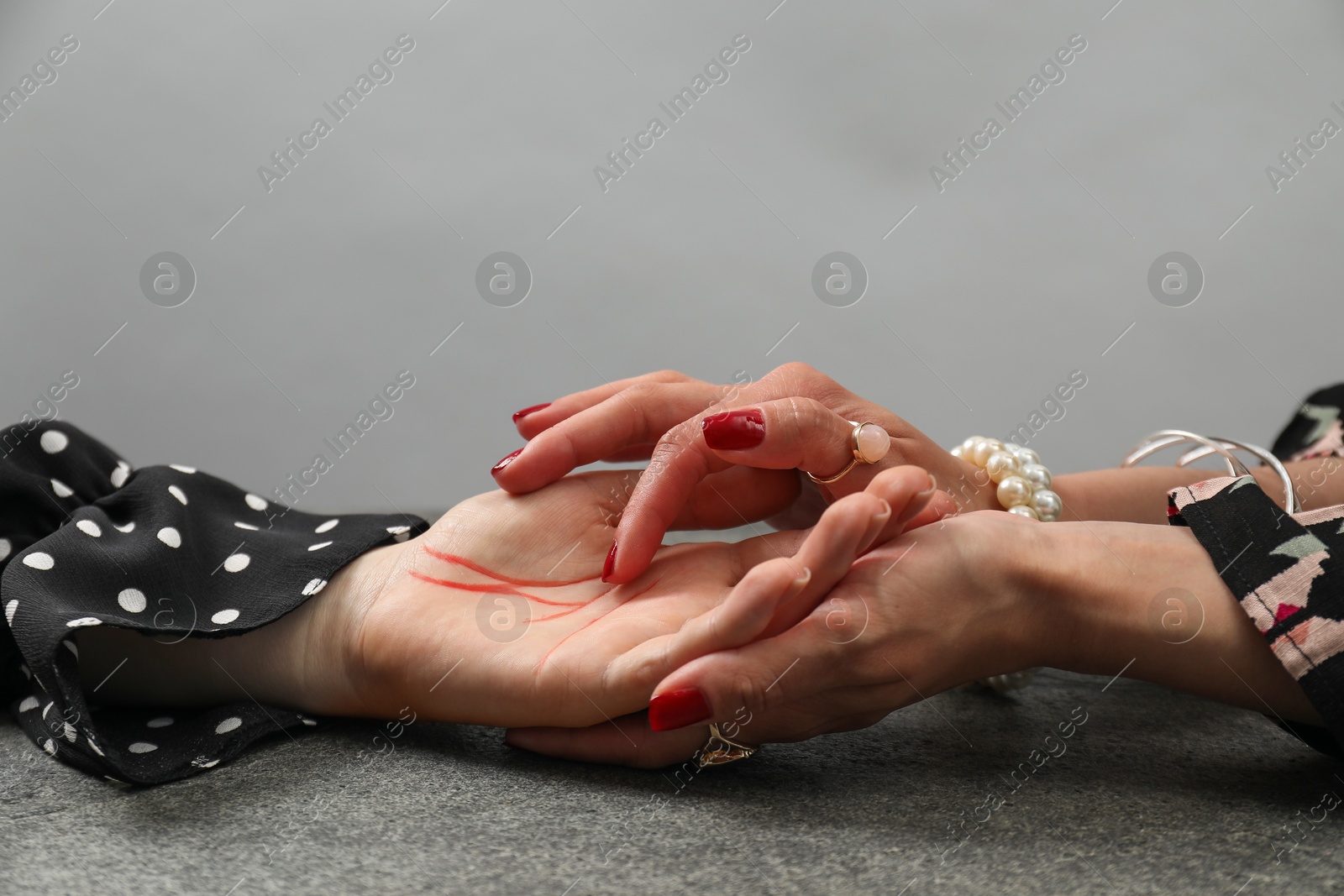 Photo of Fortune teller reading lines on woman's palm at grey table, closeup. Chiromancy