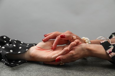 Photo of Fortune teller reading lines on woman's palm at grey table, closeup. Chiromancy