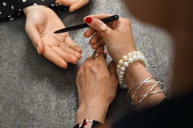 Fortune teller reading lines on woman's palm at grey table, closeup. Chiromancy