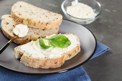 Photo of Pieces of bread with cream cheese and basil leaves on gray textured table, closeup