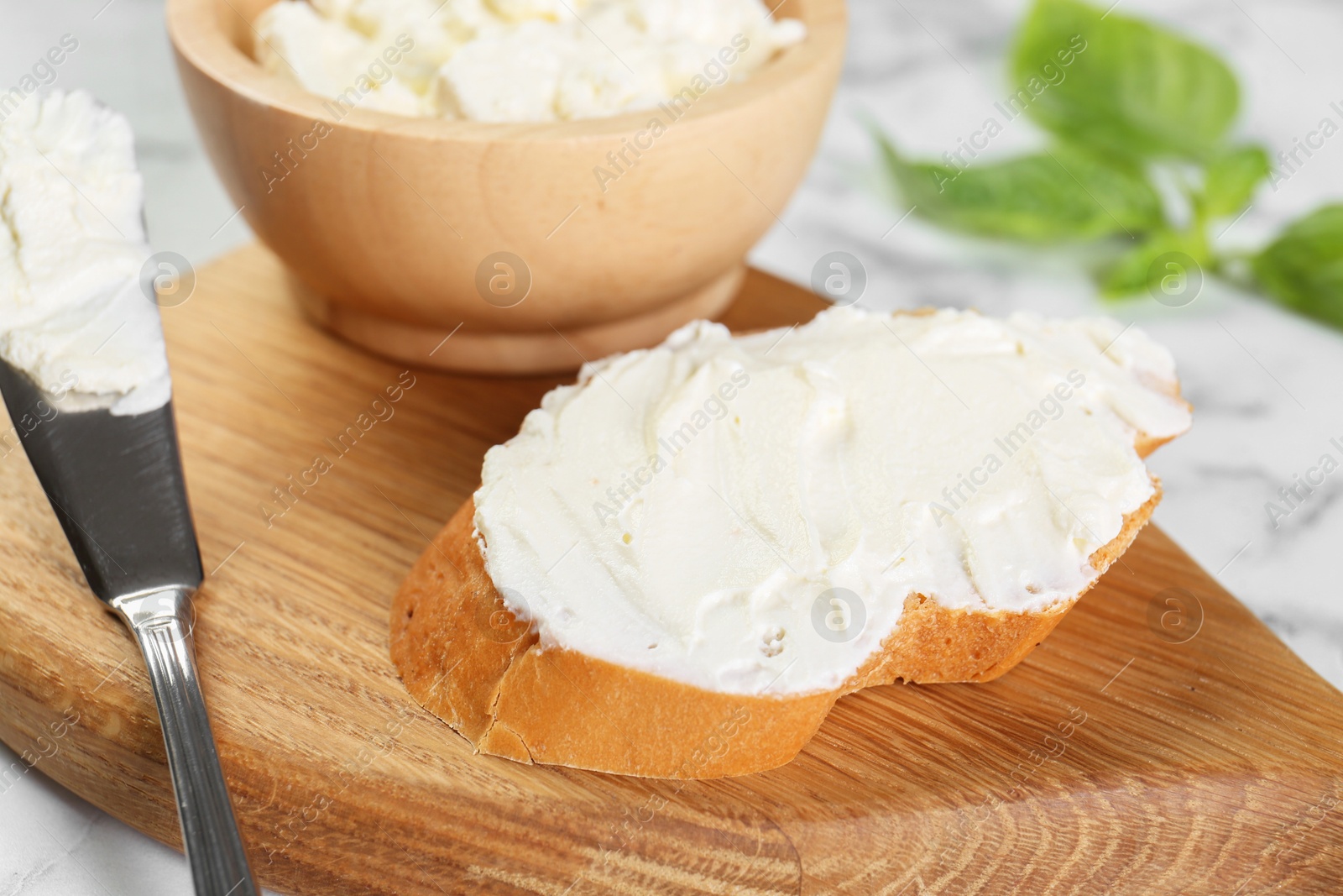 Photo of Piece of bread with cream cheese and knife on white marble table