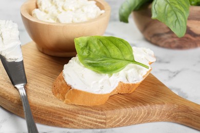 Piece of bread with cream cheese, basil and knife on white marble table