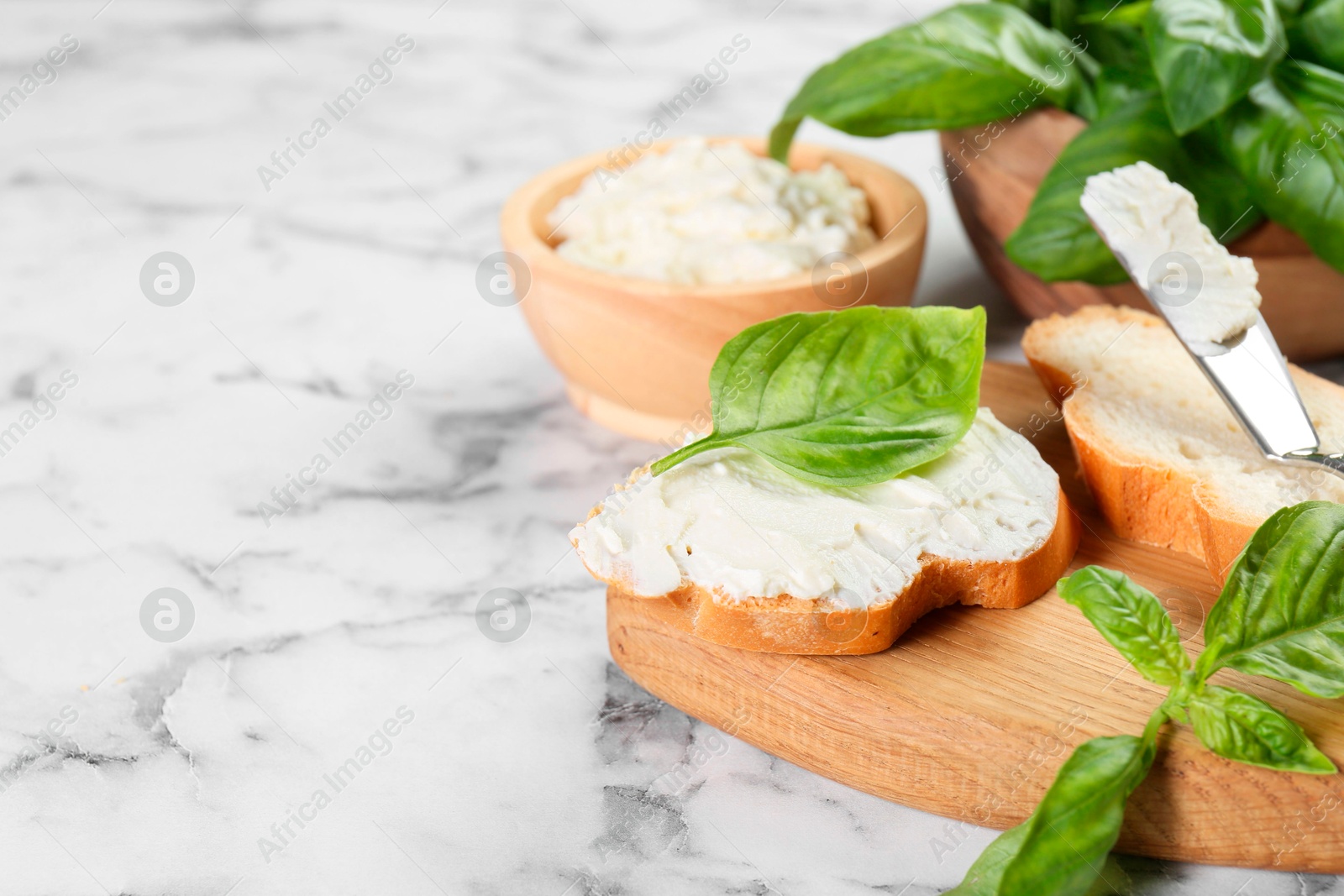 Photo of Pieces of bread with cream cheese and basil leaves on white marble table, space for text