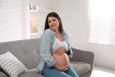 Photo of Beautiful pregnant woman sitting on sofa at home