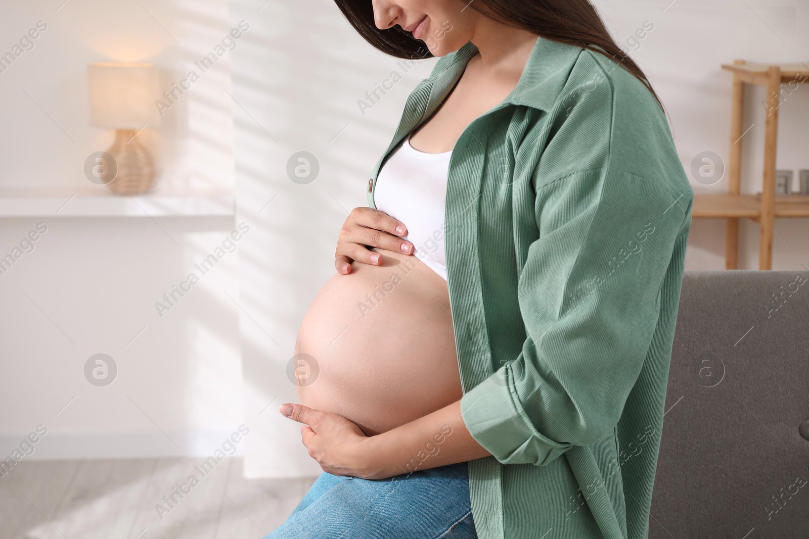 Photo of Pregnant woman sitting on sofa at home, closeup