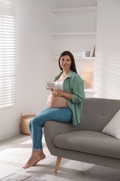 Beautiful pregnant woman sitting on sofa at home