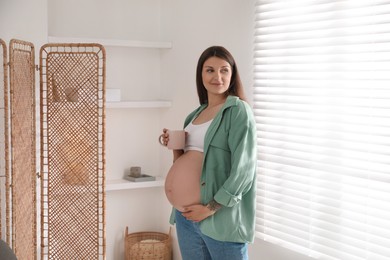 Beautiful pregnant woman with cup at home