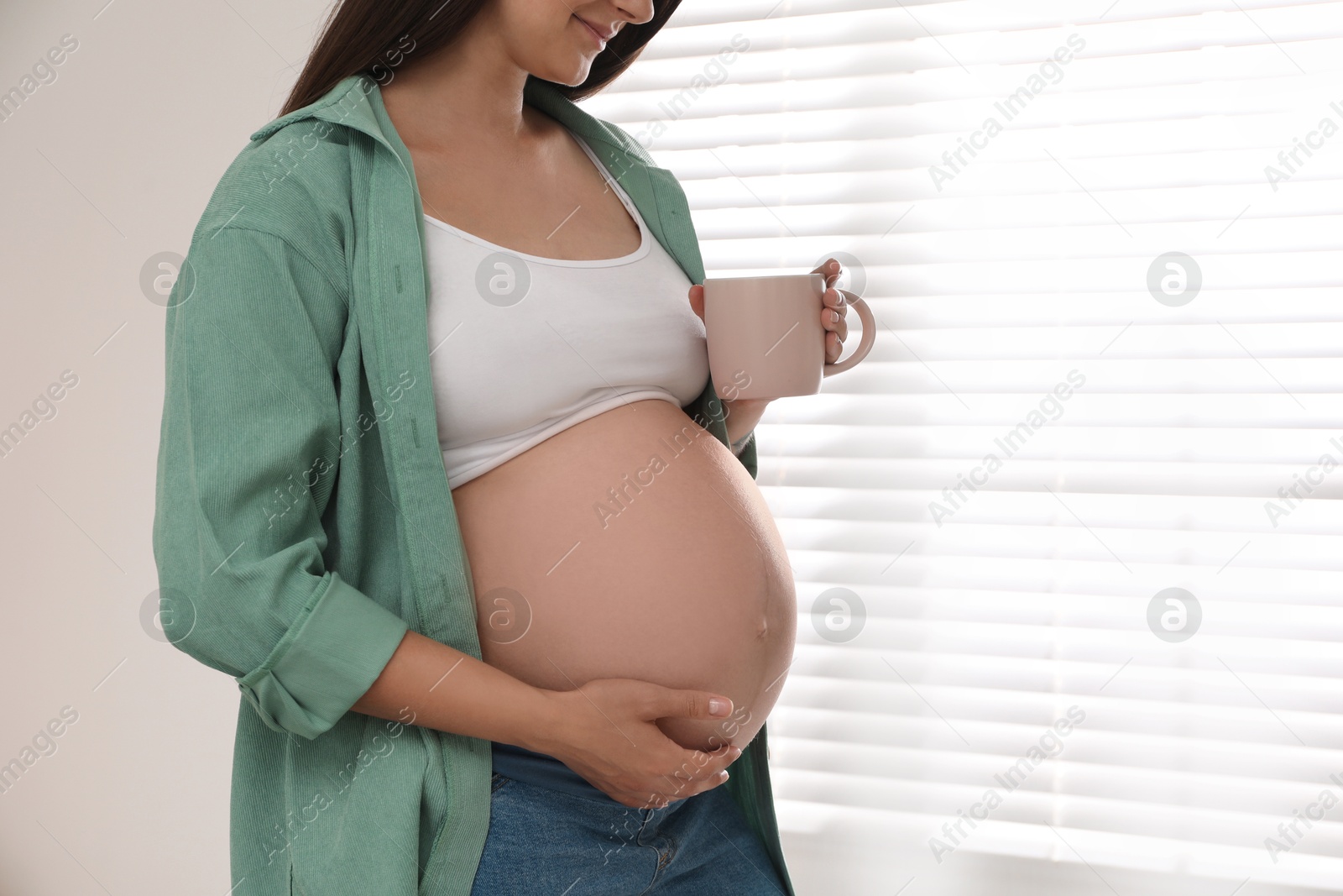 Photo of Pregnant woman with cup at home, closeup