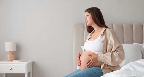 Beautiful pregnant woman on bed at home, space for text