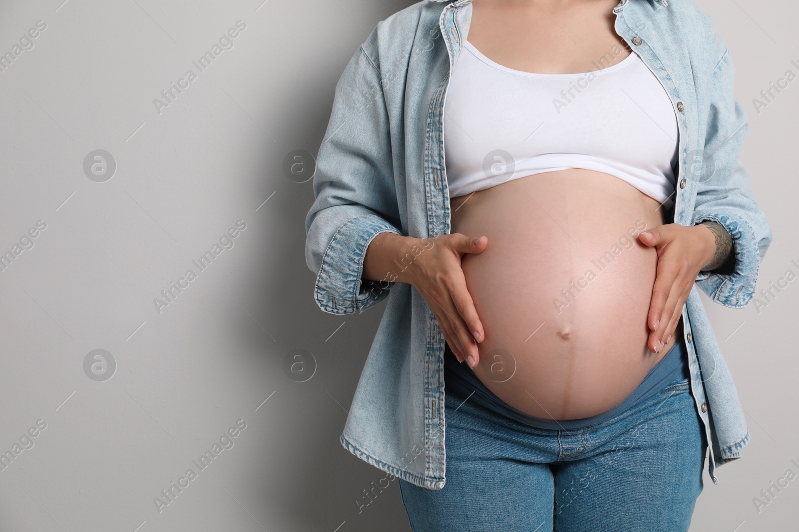 Photo of Pregnant woman on gray background, closeup. Space for text