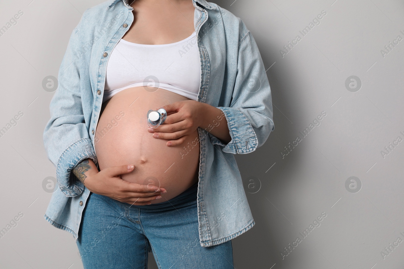 Photo of Pregnant woman with pacifier on gray background, closeup. Space for text