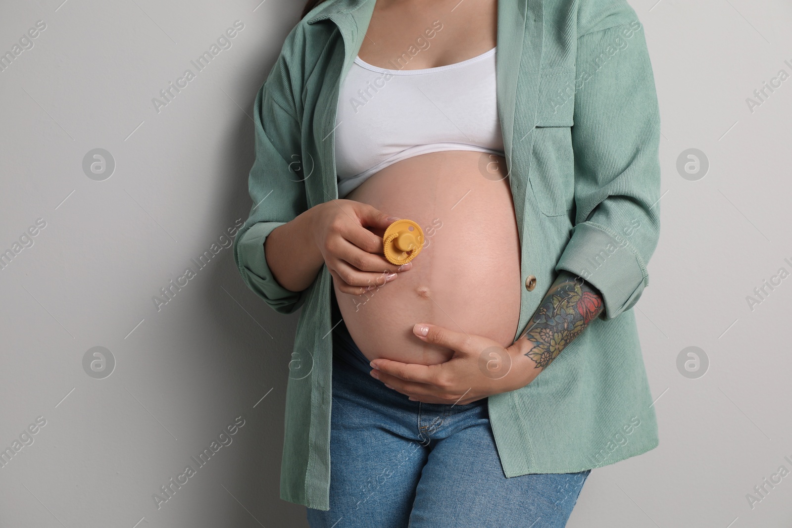 Photo of Pregnant woman with pink pacifier on gray background, closeup