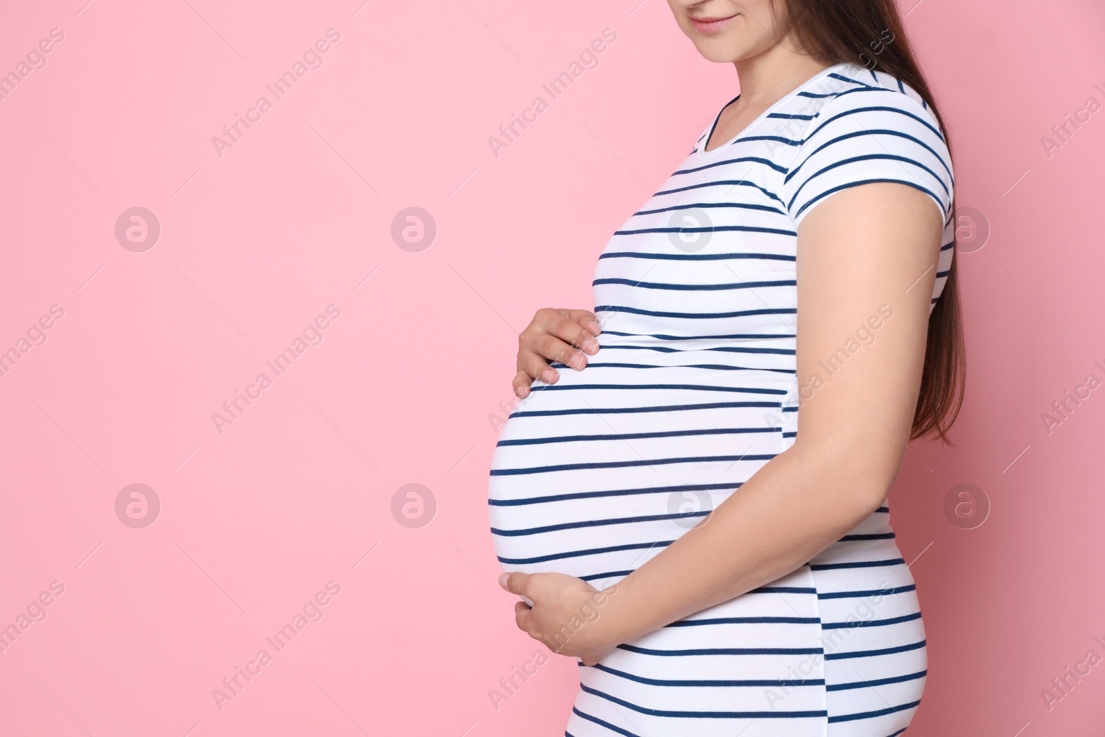 Photo of Pregnant woman on pink background, closeup. Space for text