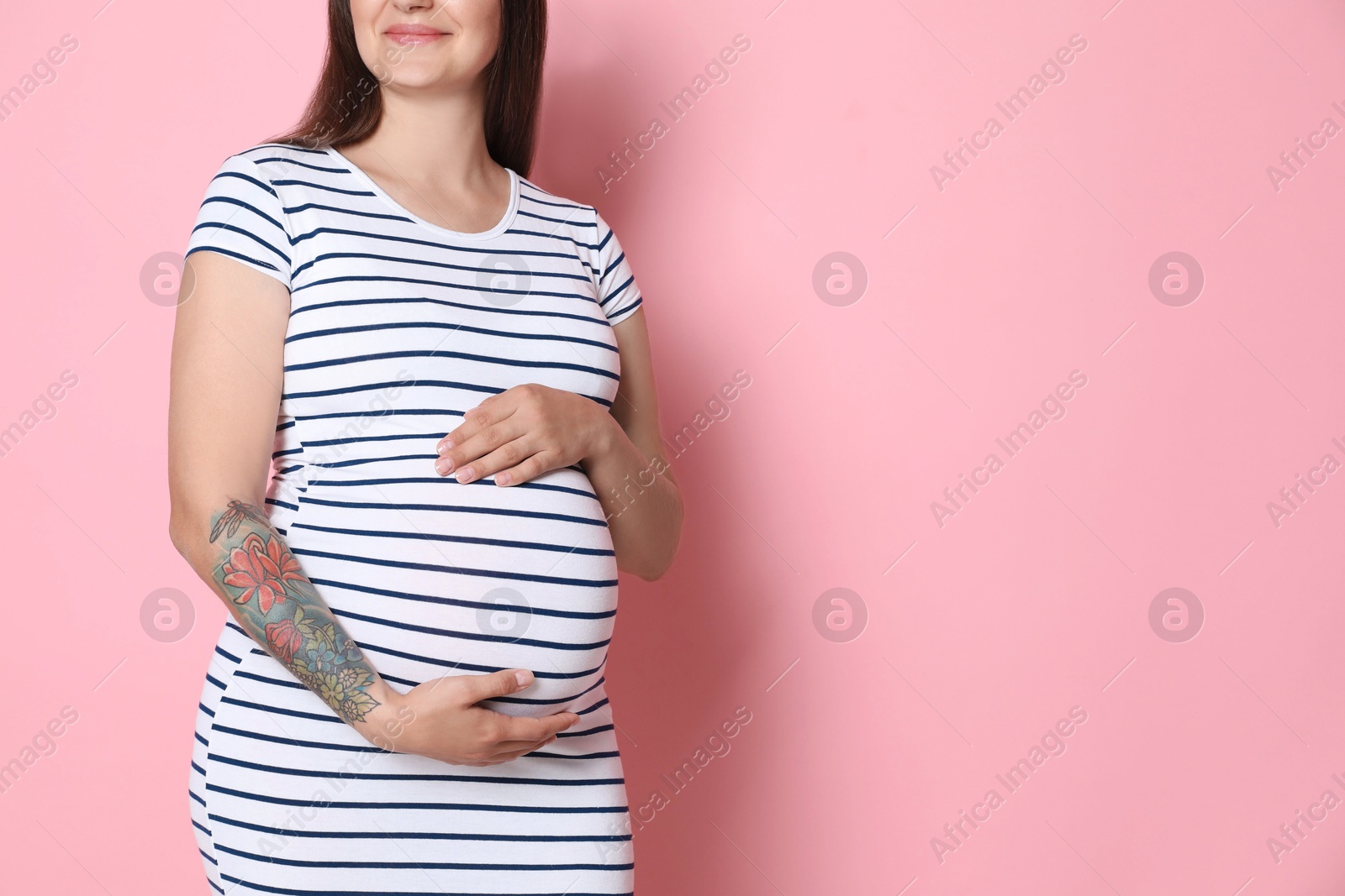 Photo of Pregnant woman on pink background, closeup. Space for text