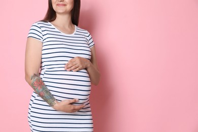 Photo of Pregnant woman on pink background, closeup. Space for text