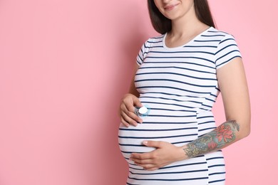 Photo of Pregnant woman with pacifier on pink background, closeup. Space for text